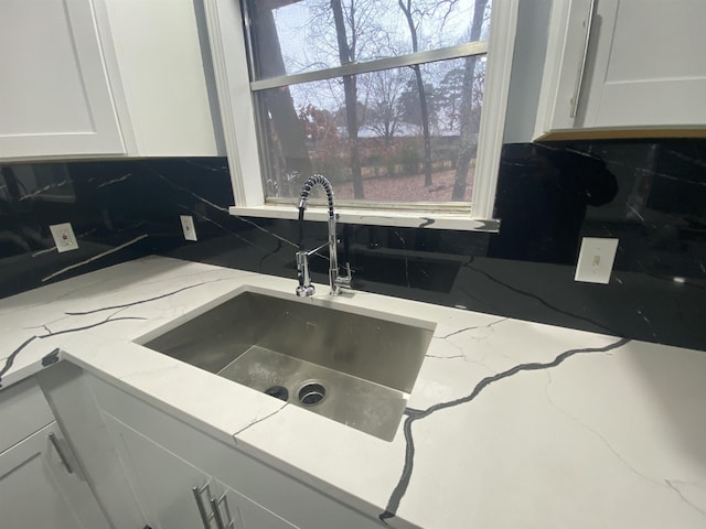 kitchen featuring light stone countertops, sink, white cabinets, and backsplash