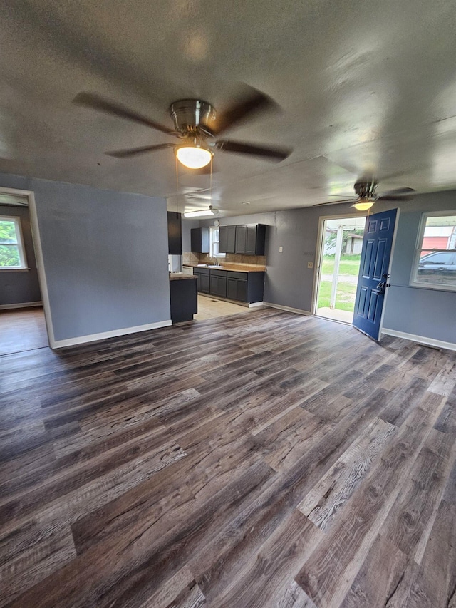 unfurnished living room with ceiling fan, a textured ceiling, and dark hardwood / wood-style flooring