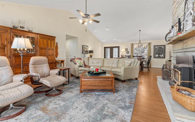 living room with light wood-type flooring, ceiling fan with notable chandelier, and high vaulted ceiling