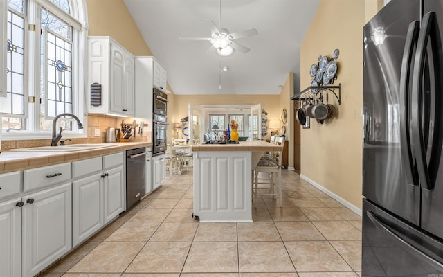 kitchen featuring a kitchen bar, tile counters, a kitchen island, stainless steel appliances, and white cabinets