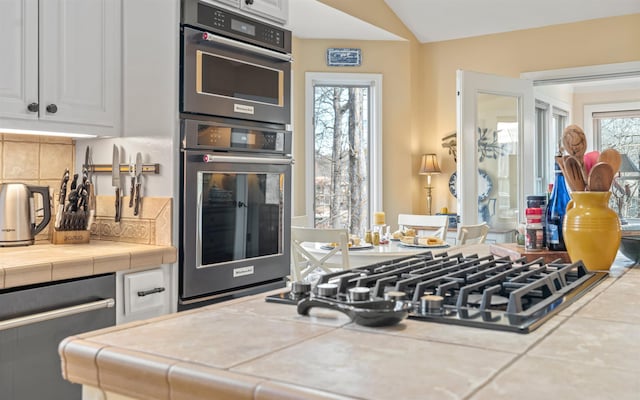 kitchen with plenty of natural light, lofted ceiling, tile counters, and white cabinets