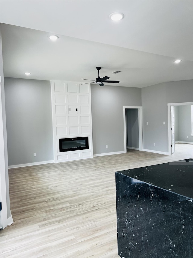 unfurnished living room with ceiling fan, a large fireplace, and light wood-type flooring