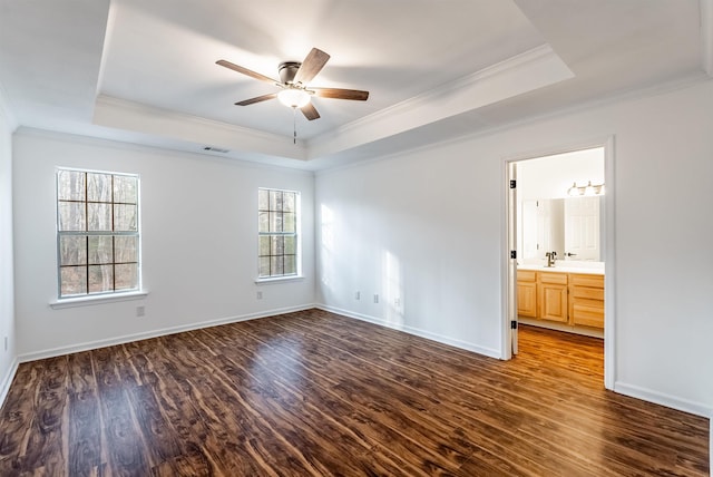 unfurnished bedroom featuring dark wood-type flooring, sink, crown molding, ensuite bath, and a raised ceiling