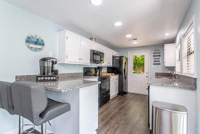 kitchen with sink, a breakfast bar, light stone counters, black appliances, and white cabinets