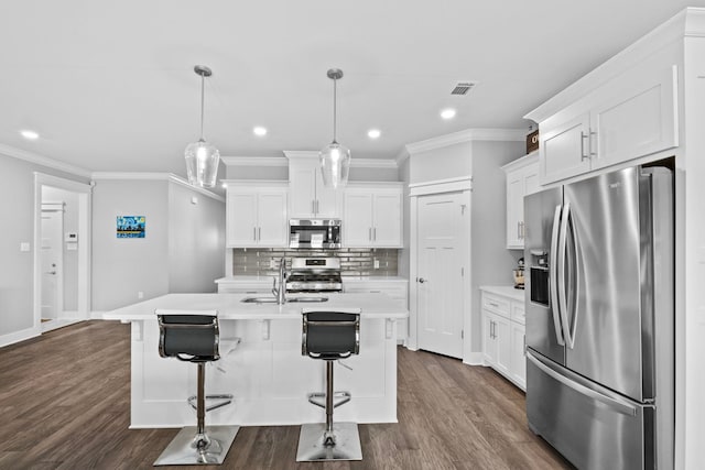 kitchen featuring a center island with sink, appliances with stainless steel finishes, hanging light fixtures, and white cabinets