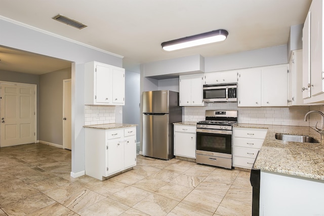 kitchen with appliances with stainless steel finishes, white cabinetry, sink, decorative backsplash, and light stone countertops