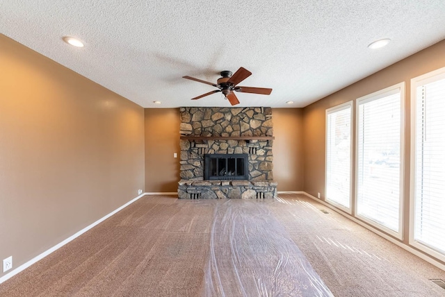 unfurnished living room featuring a stone fireplace, carpet floors, a textured ceiling, and ceiling fan