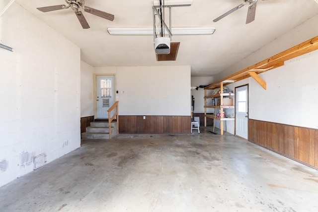 garage featuring a garage door opener, ceiling fan, and wood walls