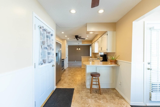 kitchen with sink, a breakfast bar, ceiling fan, white cabinetry, and kitchen peninsula