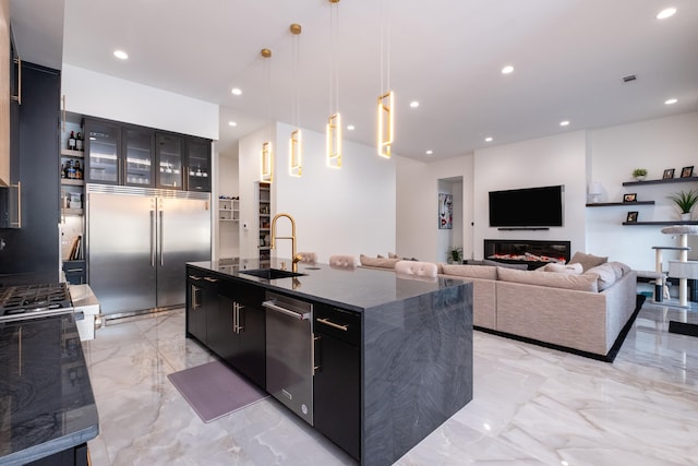 kitchen with decorative light fixtures, an island with sink, sink, dark stone countertops, and built in refrigerator