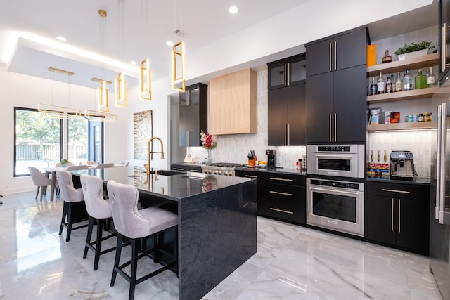 kitchen featuring decorative light fixtures, tasteful backsplash, sink, a kitchen bar, and a kitchen island with sink