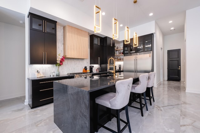 kitchen with decorative light fixtures, an island with sink, sink, dark stone countertops, and decorative backsplash