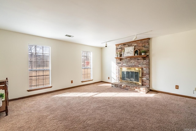 unfurnished living room with light colored carpet, track lighting, and a brick fireplace