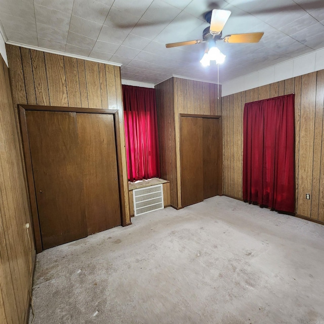 unfurnished bedroom featuring ceiling fan, wooden walls, and light colored carpet