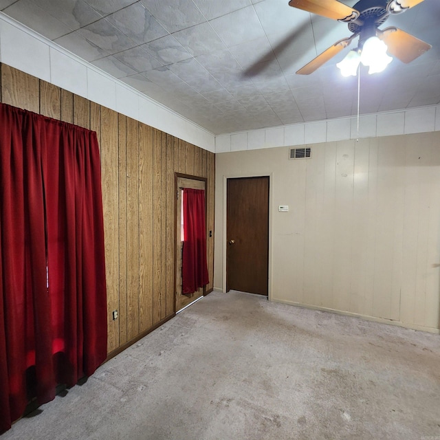 spare room with light carpet, ceiling fan, and wood walls