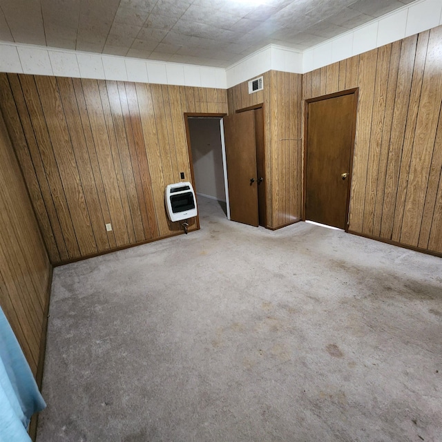 spare room featuring light colored carpet, heating unit, and wood walls