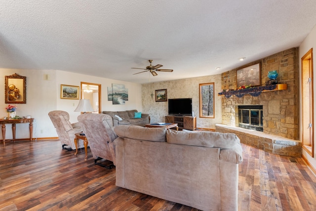 living room featuring ceiling fan, a stone fireplace, dark hardwood / wood-style floors, and a textured ceiling