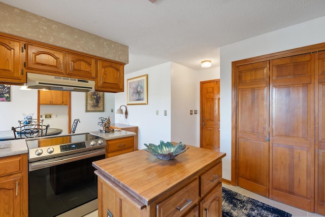 kitchen with stainless steel electric stove, a kitchen island, light tile patterned flooring, and a textured ceiling