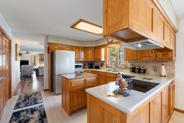 kitchen featuring sink, stainless steel refrigerator, backsplash, a center island, and kitchen peninsula