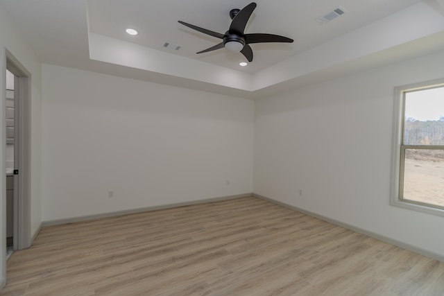 spare room featuring ceiling fan, a tray ceiling, and light hardwood / wood-style floors