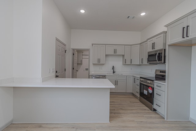 kitchen with gray cabinets, sink, kitchen peninsula, stainless steel appliances, and light hardwood / wood-style flooring