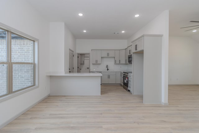 kitchen with sink, light hardwood / wood-style floors, kitchen peninsula, and appliances with stainless steel finishes