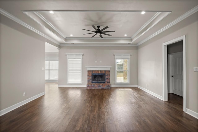 unfurnished living room with crown molding, a tray ceiling, a fireplace, and dark wood-type flooring