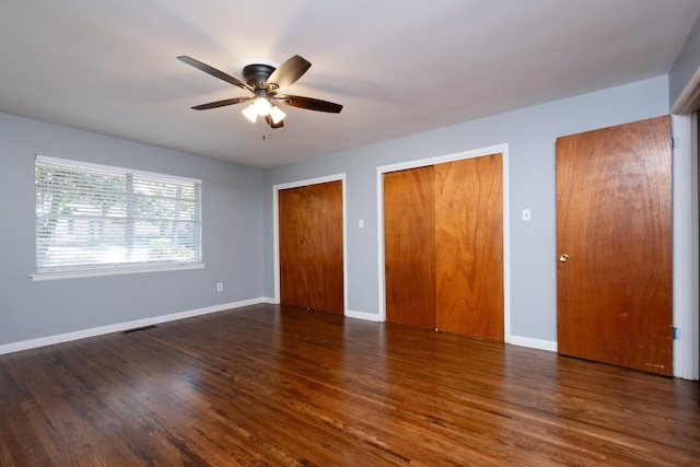 unfurnished bedroom with dark hardwood / wood-style floors, two closets, and ceiling fan