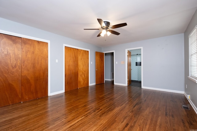 unfurnished bedroom featuring ceiling fan, dark hardwood / wood-style floors, and multiple closets