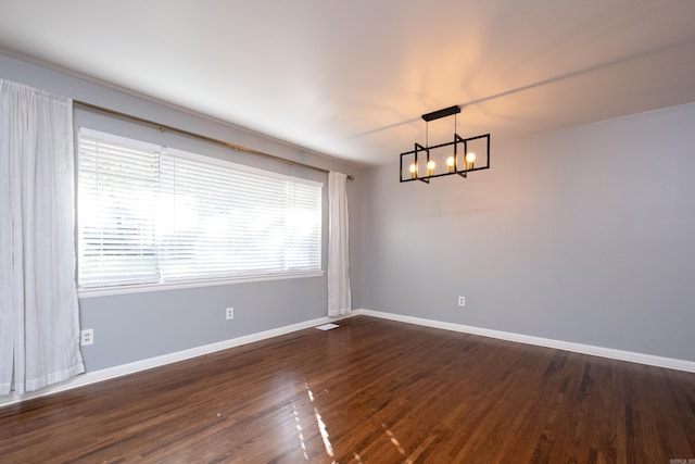 spare room with dark wood-type flooring and a notable chandelier