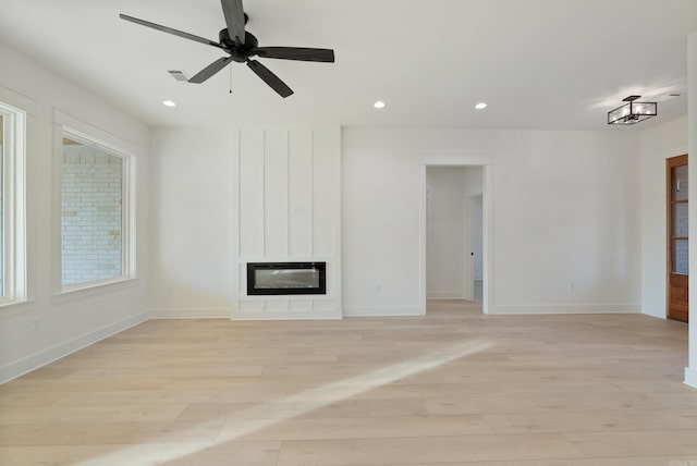 unfurnished living room featuring heating unit, a large fireplace, ceiling fan, and light wood-type flooring