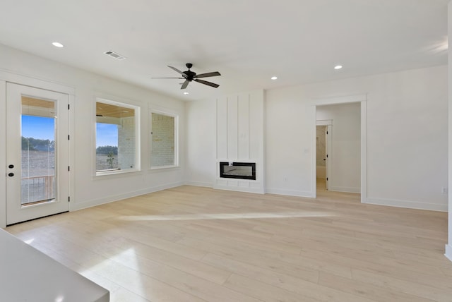 unfurnished living room featuring ceiling fan, a large fireplace, and light wood-type flooring