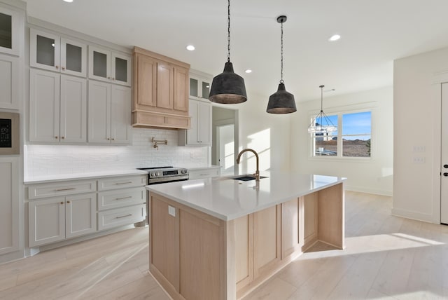 kitchen featuring sink, tasteful backsplash, a kitchen island with sink, pendant lighting, and light hardwood / wood-style floors