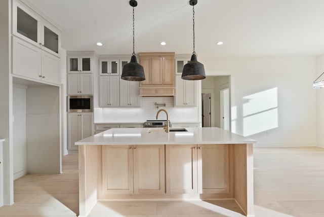 kitchen featuring stainless steel microwave, tasteful backsplash, white cabinetry, sink, and a kitchen island with sink