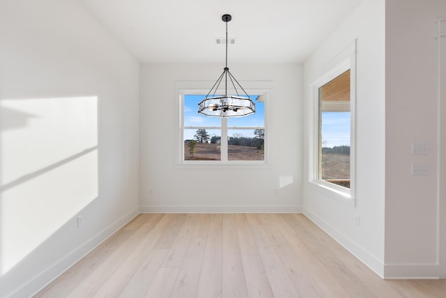 unfurnished dining area with an inviting chandelier and light wood-type flooring