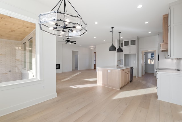 kitchen with pendant lighting, sink, light hardwood / wood-style flooring, white cabinets, and a center island with sink