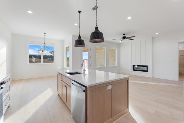 kitchen with sink, hanging light fixtures, stainless steel dishwasher, a large fireplace, and a kitchen island with sink