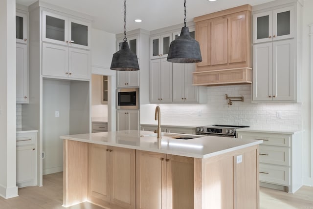 kitchen with built in microwave, stainless steel range with electric cooktop, white cabinetry, decorative light fixtures, and a kitchen island with sink