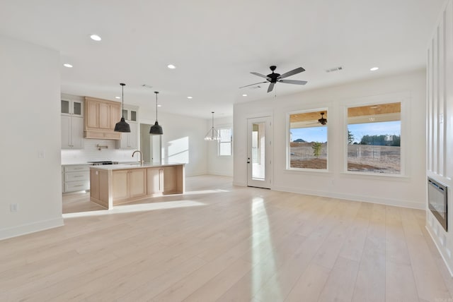 kitchen featuring decorative light fixtures, sink, decorative backsplash, a large island with sink, and light hardwood / wood-style floors