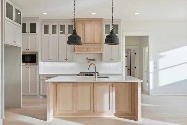 kitchen featuring sink, backsplash, hanging light fixtures, and a center island with sink