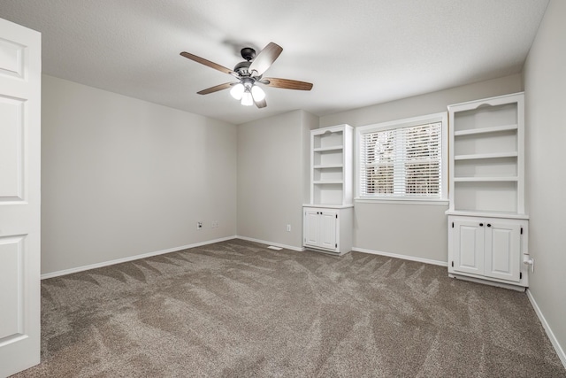 empty room featuring ceiling fan, dark carpet, and a textured ceiling