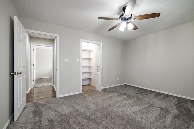 unfurnished bedroom featuring ceiling fan, a walk in closet, a textured ceiling, and dark colored carpet