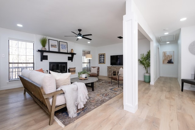 living room with a brick fireplace, ceiling fan, and light hardwood / wood-style flooring