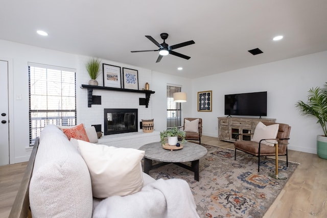 living room with ceiling fan, a wealth of natural light, a fireplace, and light wood-type flooring