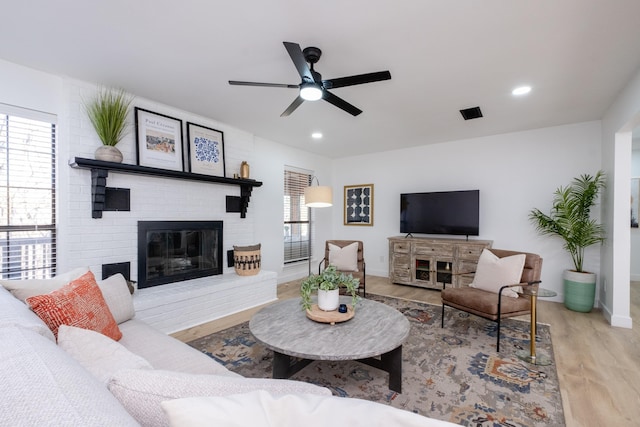 living room featuring ceiling fan, a brick fireplace, and light hardwood / wood-style flooring