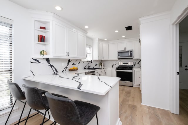 kitchen featuring sink, kitchen peninsula, white cabinets, and appliances with stainless steel finishes