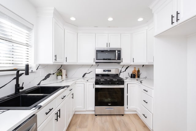 kitchen featuring sink, white cabinetry, light stone counters, light wood-type flooring, and appliances with stainless steel finishes