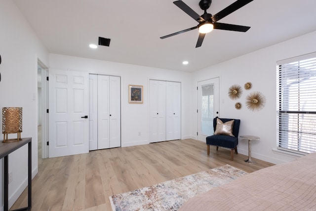 bedroom with two closets, light hardwood / wood-style flooring, and ceiling fan