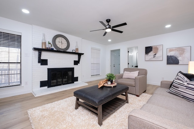 living room with ceiling fan, a brick fireplace, and light hardwood / wood-style flooring