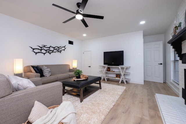 living room featuring a brick fireplace, ceiling fan, and light hardwood / wood-style flooring